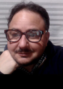 A head shot of Zosia Zaks wearing glasses with his head on his hand.
